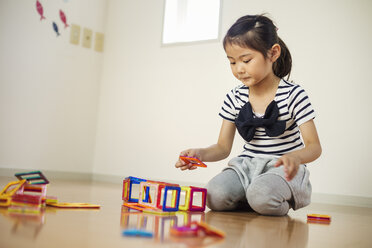 Ein Mädchen sitzt und spielt mit bunten geometrischen Formen. - MINF04740