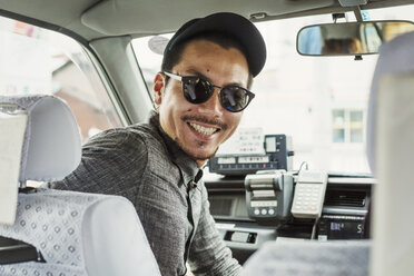 Ein Mann mit Sonnenbrille und Baseballmütze auf dem Beifahrersitz eines Autos dreht sich um und lächelt. - MINF04754