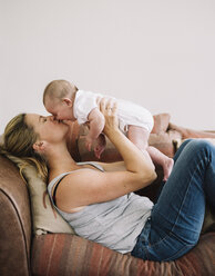 Eine Frau liegt auf einem Sofa und spielt mit einem kleinen Mädchen, das sie auf die Wange küsst. - MINF04771