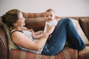 Eine Frau liegt auf einem Sofa und spielt mit einem kleinen Mädchen. - MINF04775