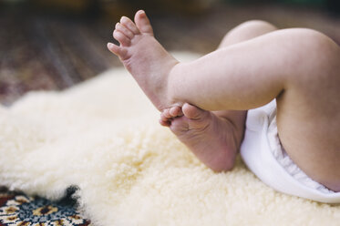 Ein Baby liegt auf einer Schafsfelldecke und strampelt mit den Beinen. - MINF04783