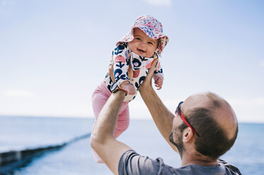 Ein Vater, der seine kleine Tochter in einem Sonnenhut in die Luft hebt, - MINF04787