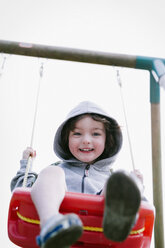 A boy in a hooded fleece, sitting on a swing - MINF04821