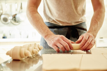 Ein Bäcker, der auf einer bemehlten Fläche Teigquadrate vor dem Backen in Croissantformen ausrollt. - MINF04831