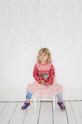 Young girl sitting on a chair in a photographers studio, posing for a picture. - MINF04880