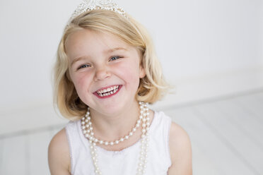 Young girl wearing a tiara and a pearl necklace, posing for a picture in a photographers studio. - MINF04888