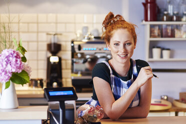Portrait of smiling young woman at the counter in a cafe - ABIF00828