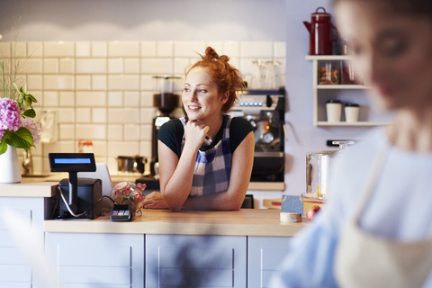 Lächelnde junge Frau an der Theke eines Cafés mit Blick zur Seite, lizenzfreies Stockfoto