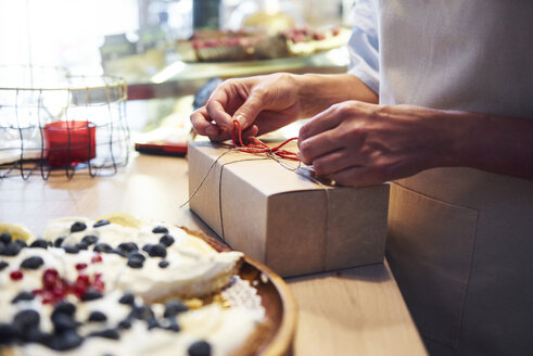Frau bindet eine Schleife an eine Kuchenschachtel in einer Konditorei - ABIF00838