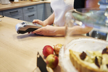 Kellnerin mit Kartenlesegerät am Tresen eines Cafés - ABIF00852