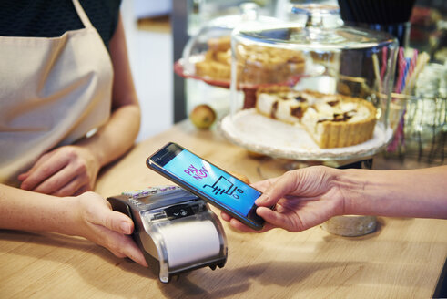Kunde zahlt bargeldlos mit Smartphone in einem Cafe - ABIF00854