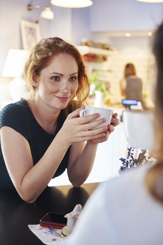 Lächelnde junge Frau trinkt Kaffee mit einem Freund in einem Café, lizenzfreies Stockfoto