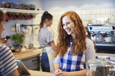 Smiling waitress talking to customer at counter in a cafe - ABIF00873