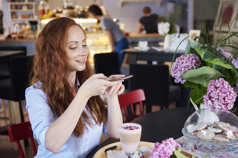 Smiling young woman taking cell phone picture of a drink in a cafe stock photo