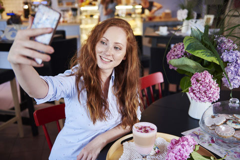 Lächelnde junge Frau macht ein Selfie in einem Café, lizenzfreies Stockfoto