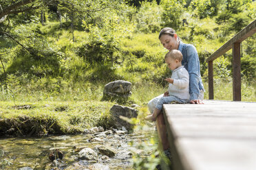 Mother and daughter sitting on wooden bridge, mountain stream - DIGF04725