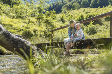 Mother and daughter sitting on wooden bridge, mountain stream - DIGF04726