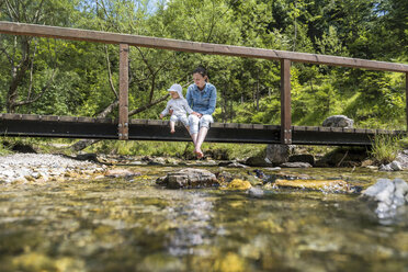 Mutter und Tochter sitzen auf einer Holzbrücke, Bergbach - DIGF04730