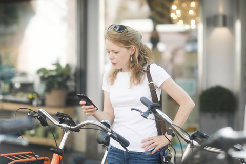 Deutschland, junge Frau mit Smartphone, die ein Stadtrad mietet, lizenzfreies Stockfoto