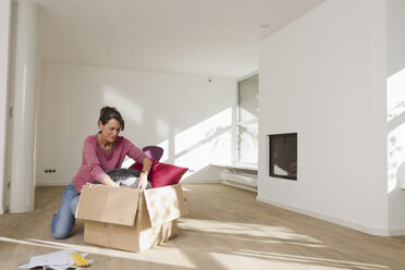 Frau beim Auspacken eines Kartons in einem leeren Raum - CUF43781