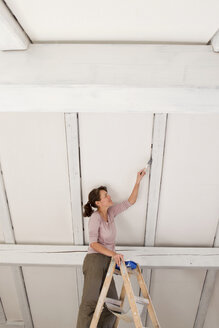 Frau auf Stehleitern beim Streichen einer weißen Decke - CUF43790
