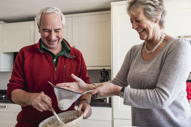 Ein älteres Ehepaar siebt das Mehl in eine Rührschüssel - CUF43816