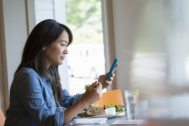 Eine Frau, die einen Salat isst und auf ihr Handy schaut. - MINF04906