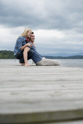 A man and woman sitting close together on a jetty by a lake. - MINF04928