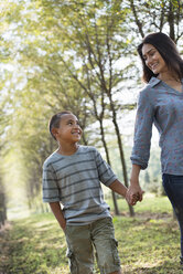 Eine Frau und ein kleiner Junge halten sich an den Händen und gehen im Wald spazieren. - MINF04976