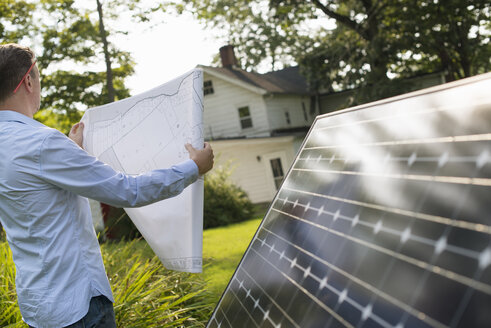 A man using a plan to place a solar panel in a farmhouse garden. - MINF04987