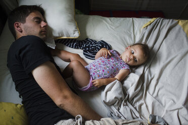 A father lying asleep on a bed beside his small daughter, view from above. - MINF04991