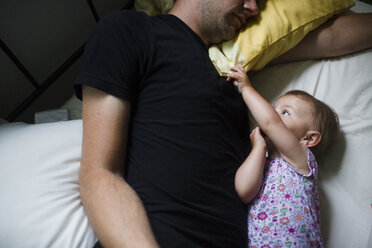Ein Vater und seine kleine Tochter liegen zusammen auf einem Bett und spielen und kitzeln sich, Blick von oben. - MINF04993