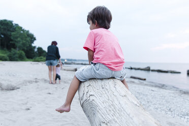 A boy sitting on a wooden breakwater in a sandy beach. - MINF04997