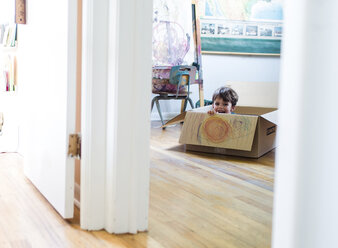 A boy sitting crouched down in a cardboard box laughing. - MINF05002