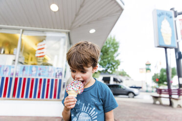 Ein Kind, ein Junge, der vor einer Eisdiele steht und eine Eiswaffel isst. - MINF05003