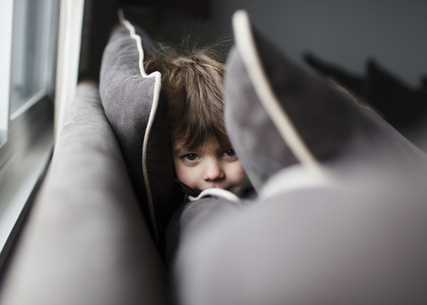 Ein Kind, ein Junge, der sich zwischen den Polstern eines Sofas versteckt., lizenzfreies Stockfoto