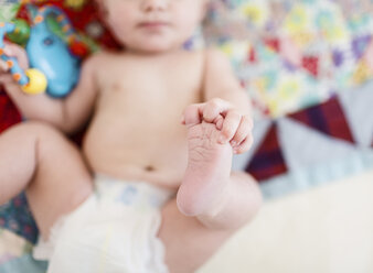 Ein kleines Mädchen, das auf einer Patchwork-Decke liegt und seine eigenen Füße hält. - MINF05011