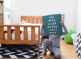 Ein Junge, ein Kind, das in einem Schlafzimmer ein Zeichen des Alphabets hochhält. - MINF05025