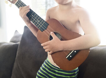 Ein Junge, ein Kind mit einer Ukulele in der Hand, sitzt auf einem Sofa. - MINF05026