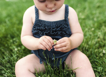 Ein kleines Mädchen sitzt und spielt mit Gras. - MINF05031