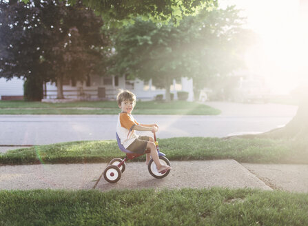 Ein Junge, der in einer Vorstadt auf einem Dreirad fährt. - MINF05035