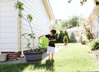 Ein Junge, ein Kind, das in einem Garten steht und eine Pflanze in einem Topf gießt. - MINF05041