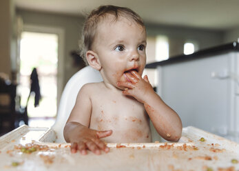 A baby girl sitting in a high chair covered in spilt food. - MINF05053