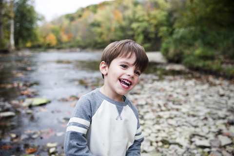 Ein Kind, ein Junge, steht am felsigen Ufer eines Flusses., lizenzfreies Stockfoto