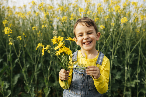 Porträt eines kleinen Jungen mit gepflückten gelben Blumen in der Natur, lizenzfreies Stockfoto