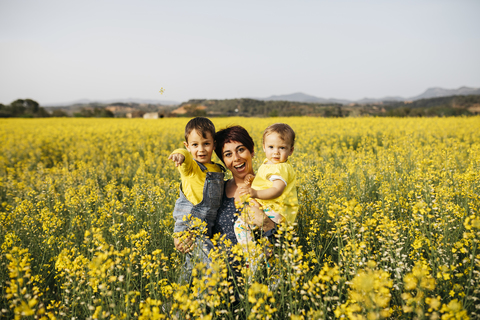 Spanien, Porträt einer lachenden Mutter mit kleinem Sohn und Tochter in einem Rapsfeld, lizenzfreies Stockfoto