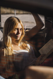 Porträt einer jungen Frau, die in einem Auto sitzt und ein Buch liest - KKAF01357