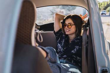 Lächelnde junge Frau mit Sonnenbrille, die in einem Auto sitzt - KKAF01358
