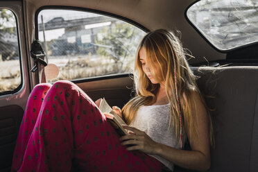 Junge Frau sitzt in einem Auto und liest ein Buch - KKAF01360