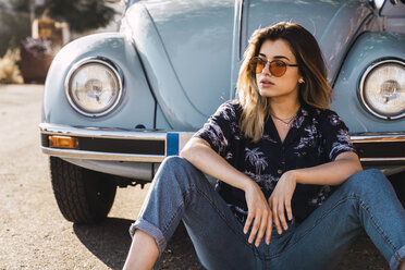 Young woman wearing sunglasses sitting outside at a vintage car - KKAF01362